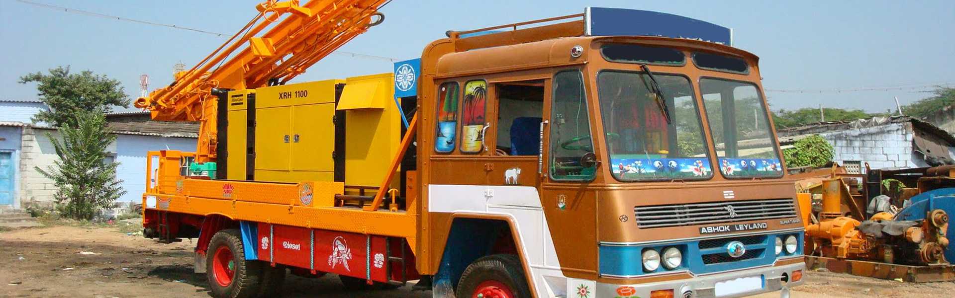 An orange truck carries a borewell machine for borewell drilling, cleaning, and flushing services